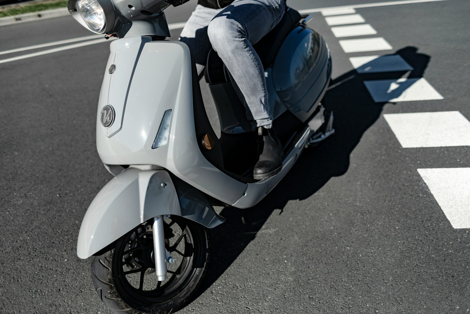 person in blue denim jeans and black socks riding on white and blue motor scooter